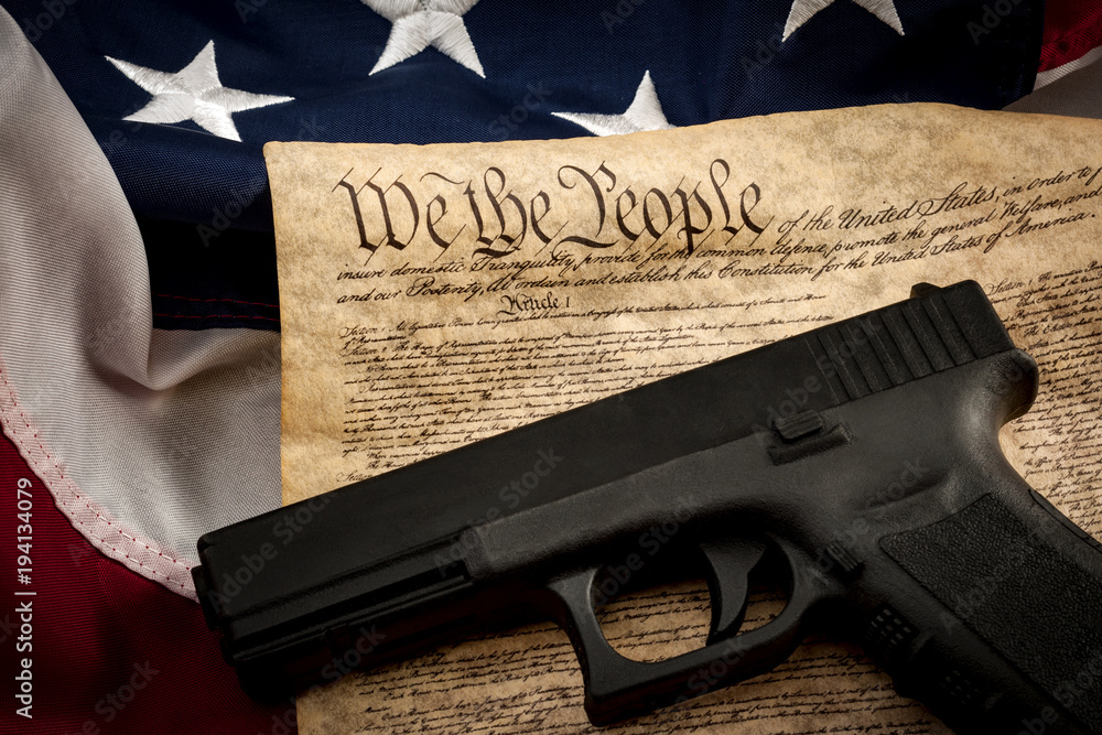 The second amendment and gun control in america concept with a handgun and the american constitution on the USA flag with close up on the "we the people" part of the united states constitution